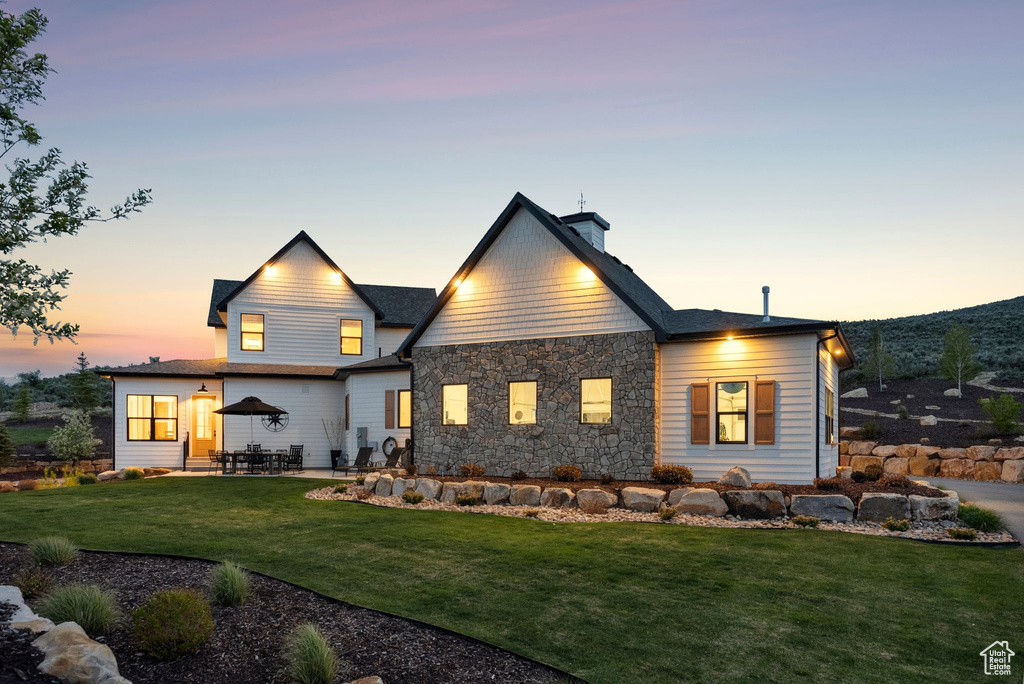 Back of property featuring a yard, a patio, stone siding, and a chimney