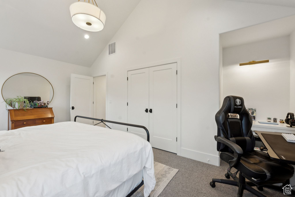 Carpeted bedroom with high vaulted ceiling, a desk, and a closet