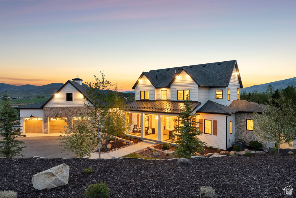 Back of property at dusk with covered porch, driveway, central AC unit, an attached garage, and a mountain view