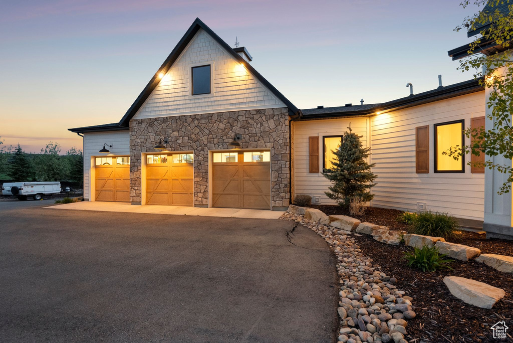 View of front of house with stone siding, driveway, and a garage