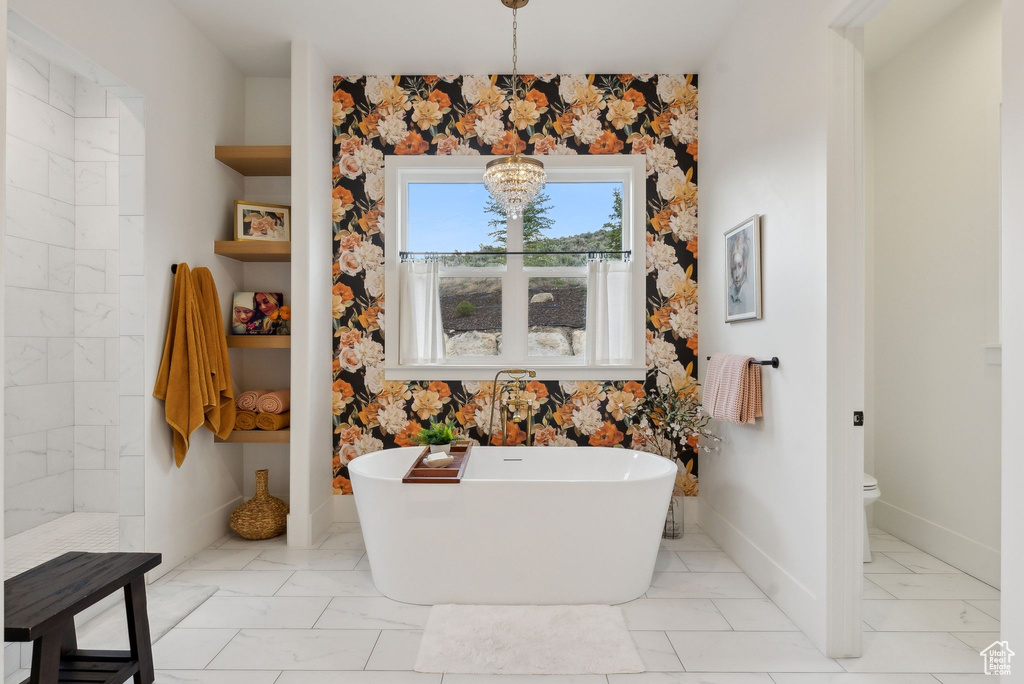 Full bathroom featuring a freestanding tub, toilet, marble finish floors, baseboards, and a chandelier