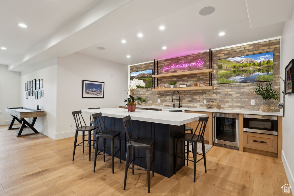 Indoor wet bar with beverage cooler, light wood-style floors, recessed lighting, stainless steel microwave, and baseboards