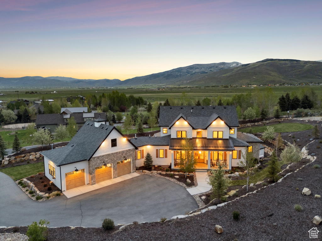 Back of property at dusk featuring a mountain view, covered porch, concrete driveway, and stone siding
