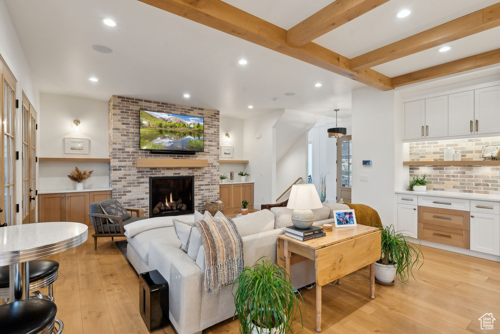Living area with light wood-style flooring, recessed lighting, beamed ceiling, and a brick fireplace