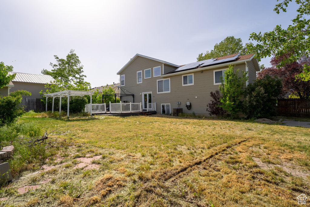 Back of house with a pergola, a wooden deck, and roof mounted solar panels