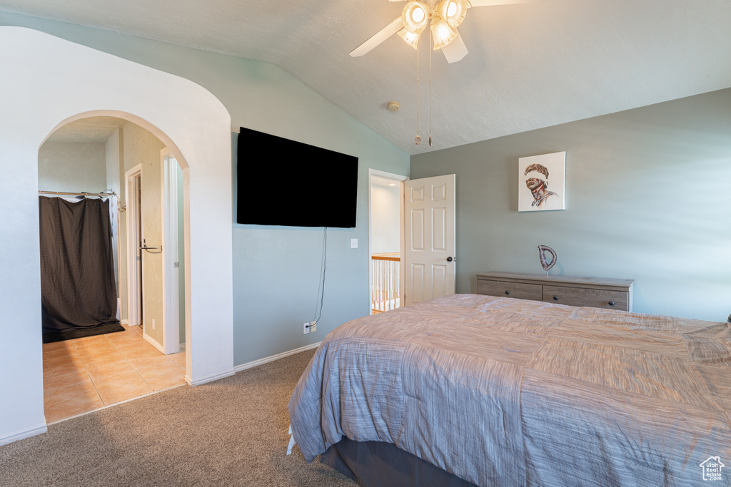 Bedroom featuring vaulted ceiling, arched walkways, carpet, tile patterned flooring, and ceiling fan