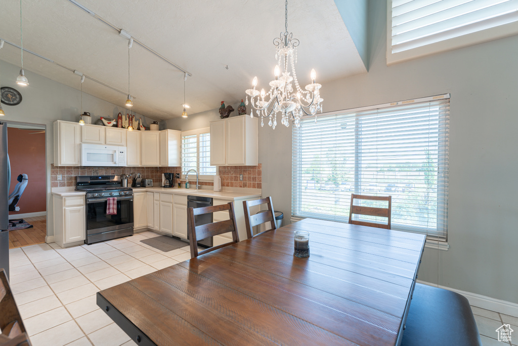 Dining space with lofted ceiling, light tile patterned floors, a chandelier, track lighting, and baseboards