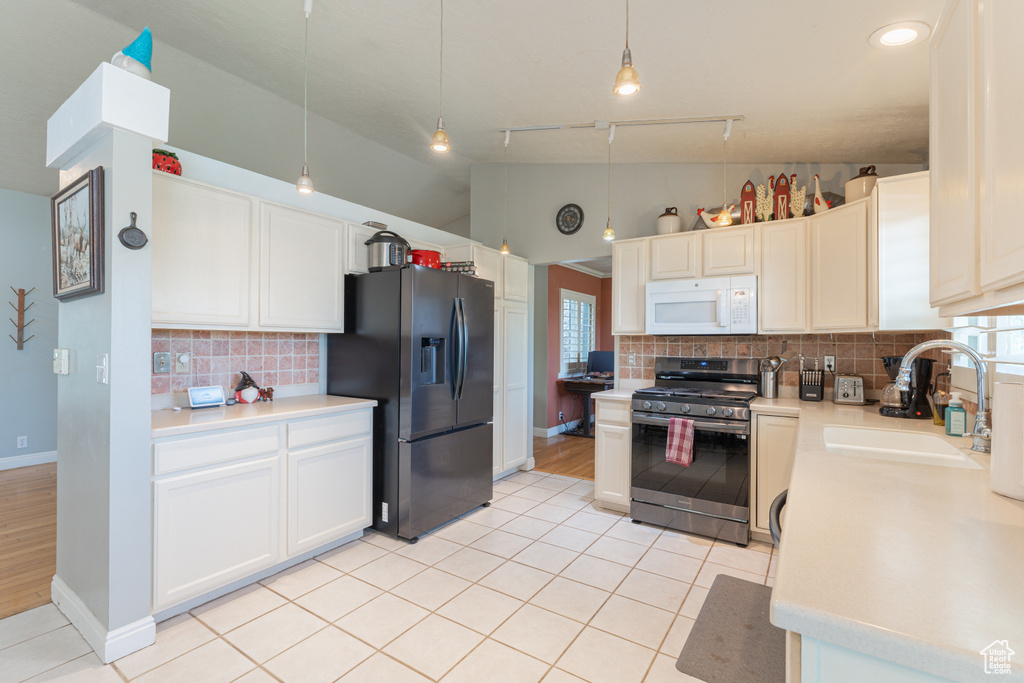 Kitchen with stainless steel gas range, refrigerator with ice dispenser, white microwave, a sink, and vaulted ceiling