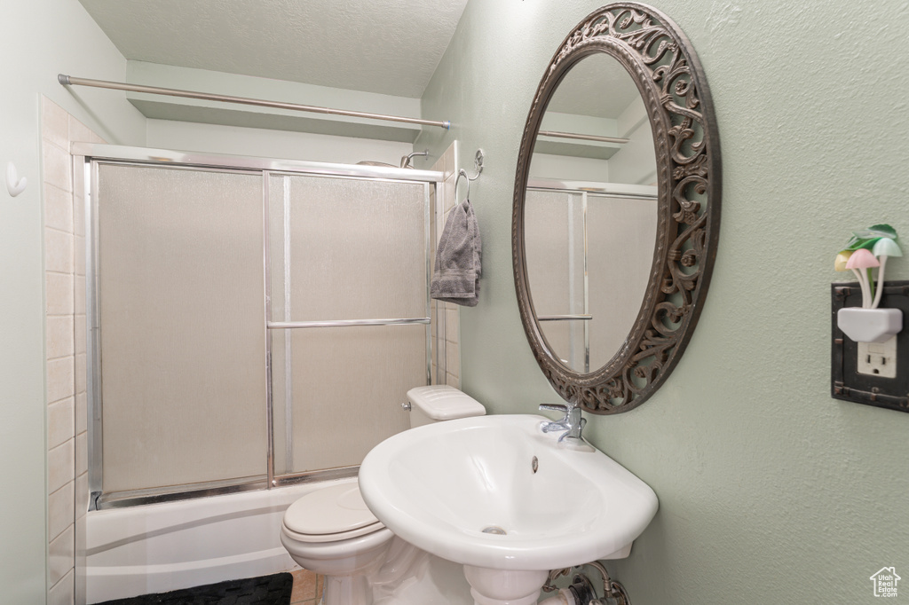 Bathroom featuring a sink, toilet, bath / shower combo with glass door, and a textured wall