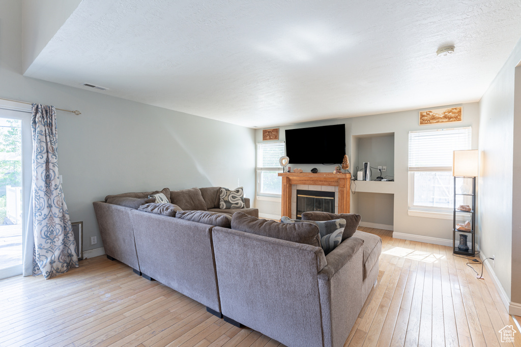 Living area with light wood-style flooring, a tiled fireplace, healthy amount of natural light, and baseboards