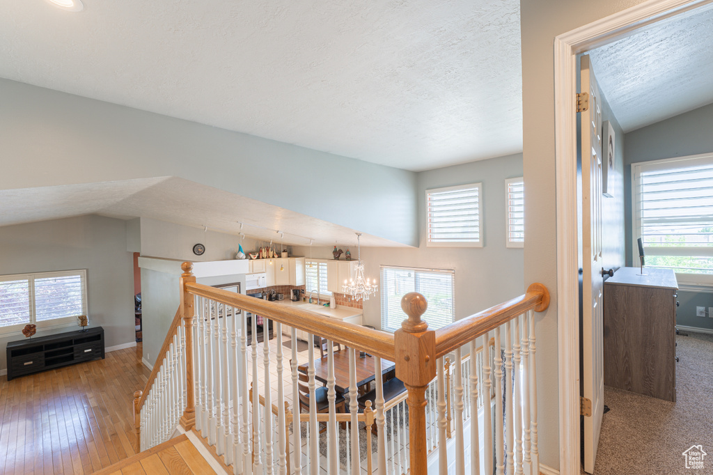 Corridor featuring an upstairs landing, healthy amount of natural light, a chandelier, and a textured ceiling