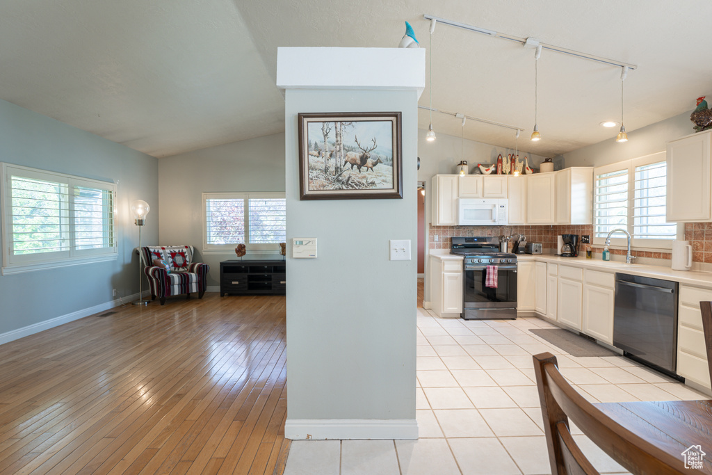 Kitchen featuring dishwasher, white microwave, stainless steel range with gas cooktop, track lighting, and vaulted ceiling
