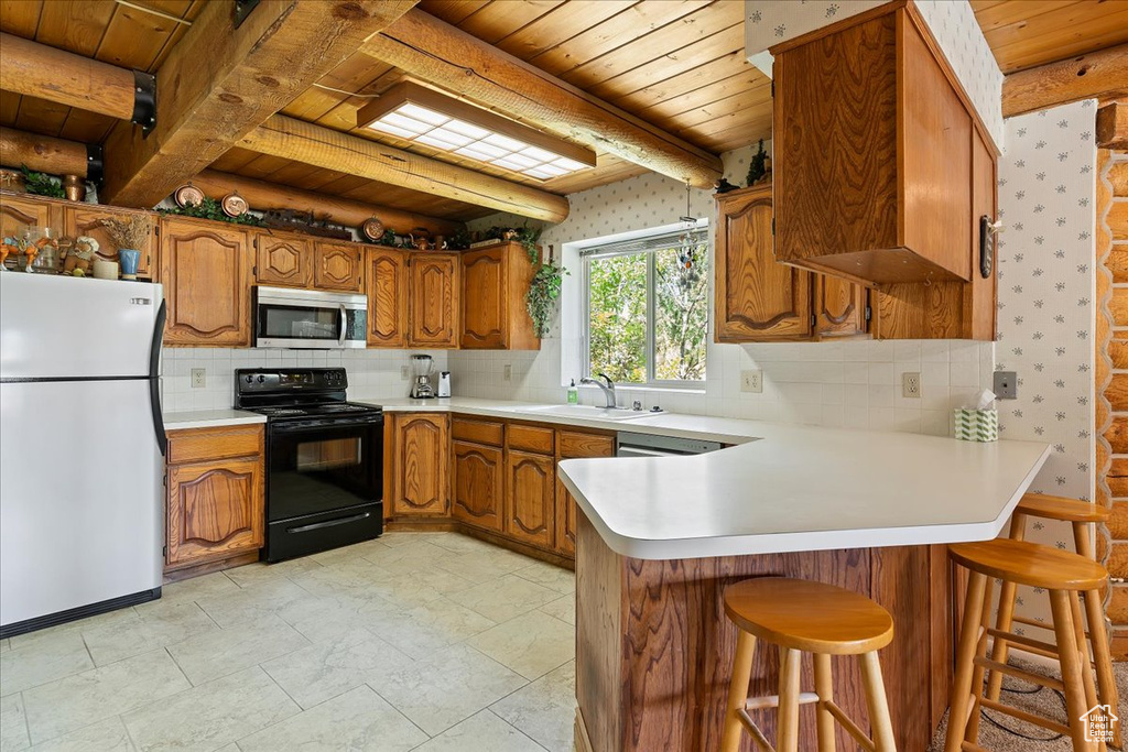 Kitchen with freestanding refrigerator, black / electric stove, stainless steel microwave, wooden ceiling, and brown cabinetry