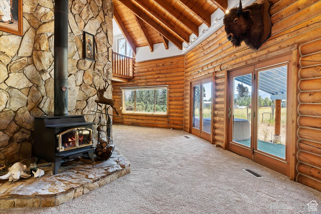 Unfurnished living room featuring carpet floors, a wood stove, wooden ceiling, beam ceiling, and log walls
