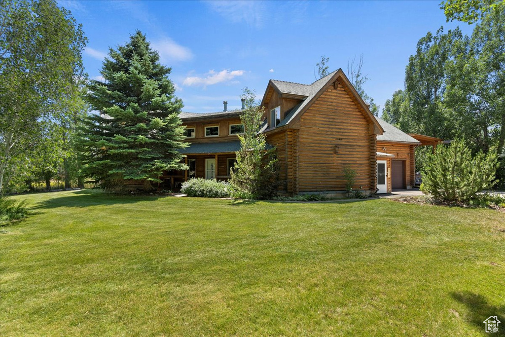 Rear view of house featuring a garage, a lawn, and log siding