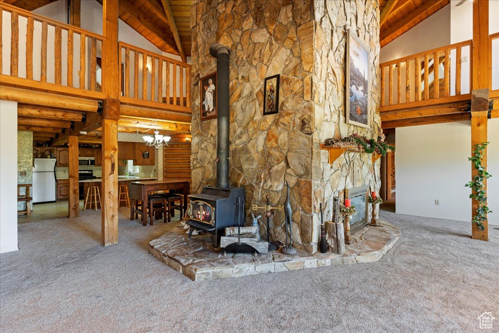 Unfurnished living room featuring carpet flooring, high vaulted ceiling, a wood stove, beam ceiling, and wood ceiling