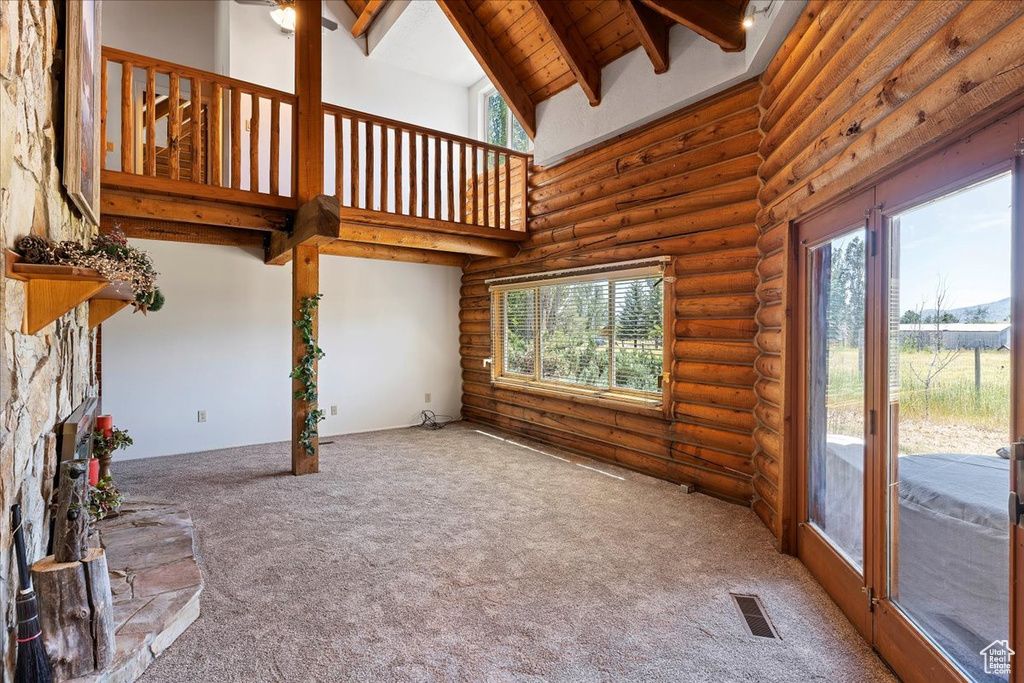 Unfurnished living room featuring log walls, plenty of natural light, carpet flooring, high vaulted ceiling, and beam ceiling