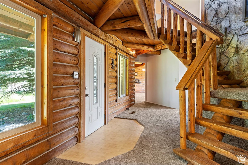 Foyer with stairway, rustic walls, beam ceiling, wooden ceiling, and carpet