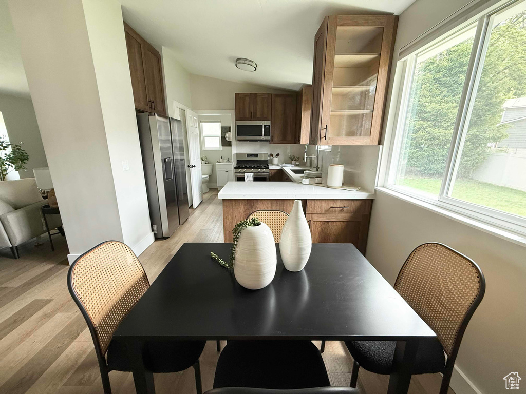 Kitchen featuring appliances with stainless steel finishes, light countertops, lofted ceiling, light wood-style floors, and a peninsula