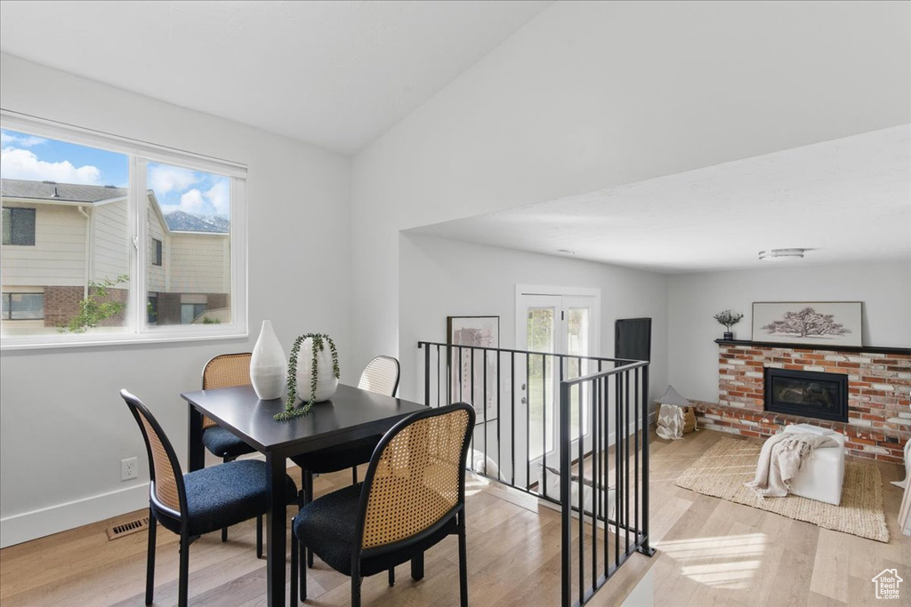Dining room with light wood-type flooring, plenty of natural light, a fireplace, baseboards, and vaulted ceiling