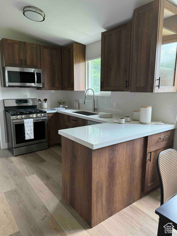 Kitchen with stainless steel appliances, a sink, light wood-type flooring, light countertops, and a peninsula