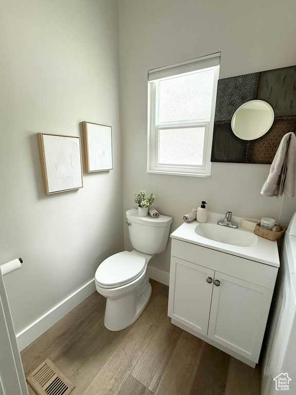 Half bath with wood finished floors, baseboards, toilet, and vanity