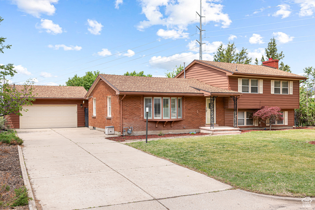 Split level home with a chimney, concrete driveway, a garage, brick siding, and a front lawn