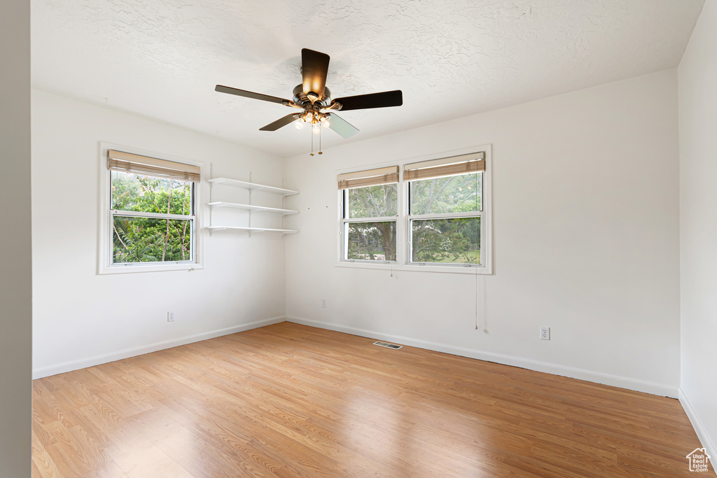 Spare room featuring light wood-style floors, baseboards, ceiling fan, and a textured ceiling