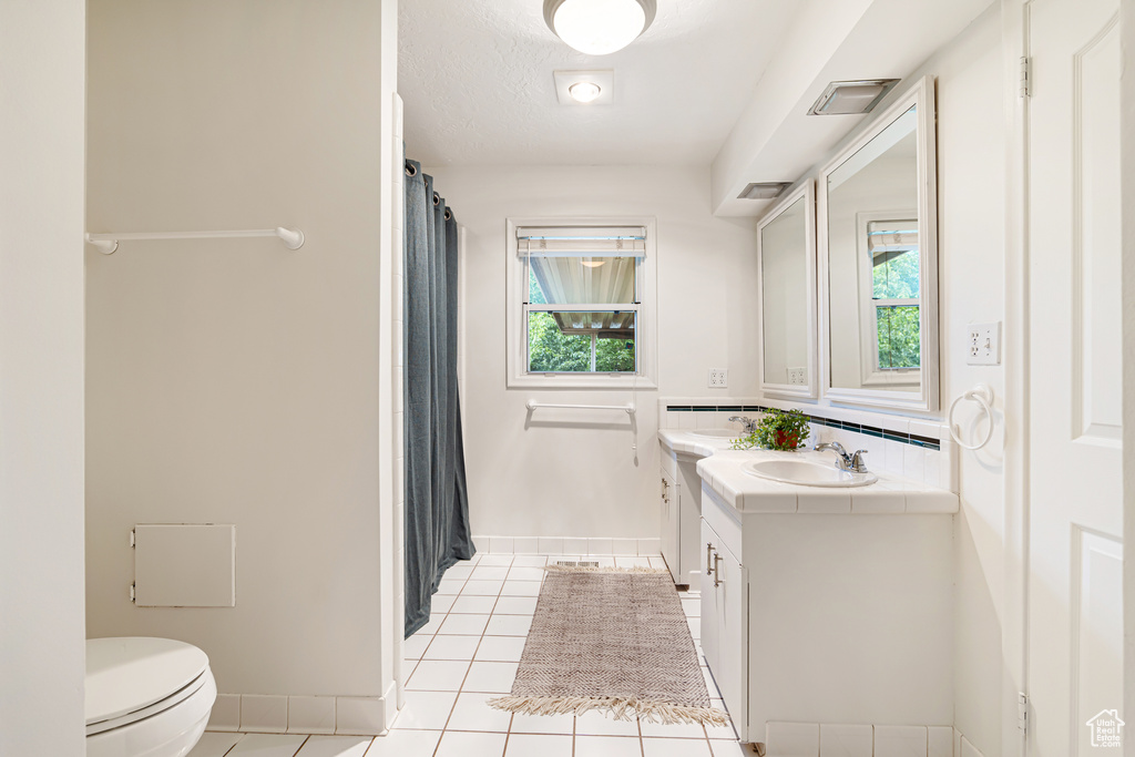 Full bath featuring toilet, healthy amount of natural light, tile patterned flooring, vanity, and a textured ceiling