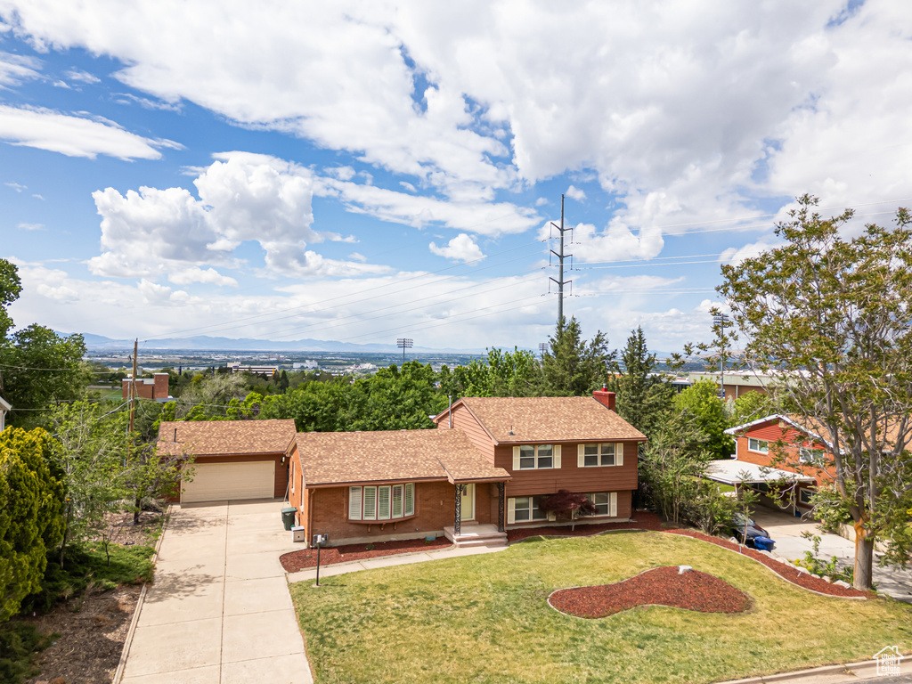 Split level home featuring driveway, a garage, a front lawn, a chimney, and brick siding