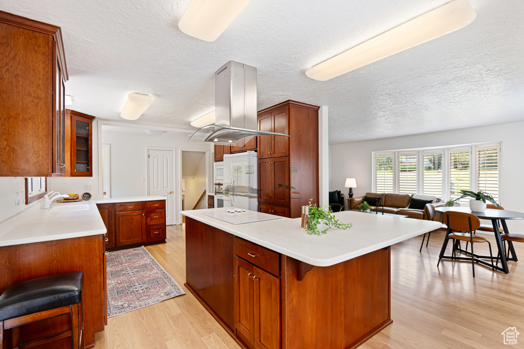 Kitchen with light wood finished floors, island range hood, a textured ceiling, glass insert cabinets, and light countertops