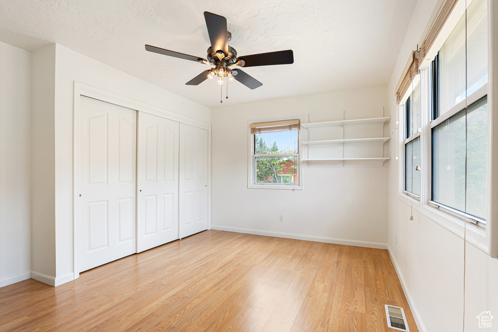 Unfurnished bedroom with light wood-style floors, baseboards, ceiling fan, a closet, and a textured ceiling