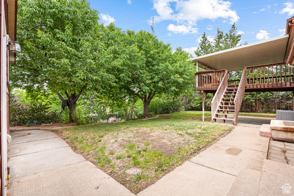View of green lawn with stairs, a wooden deck, central AC, and a patio area
