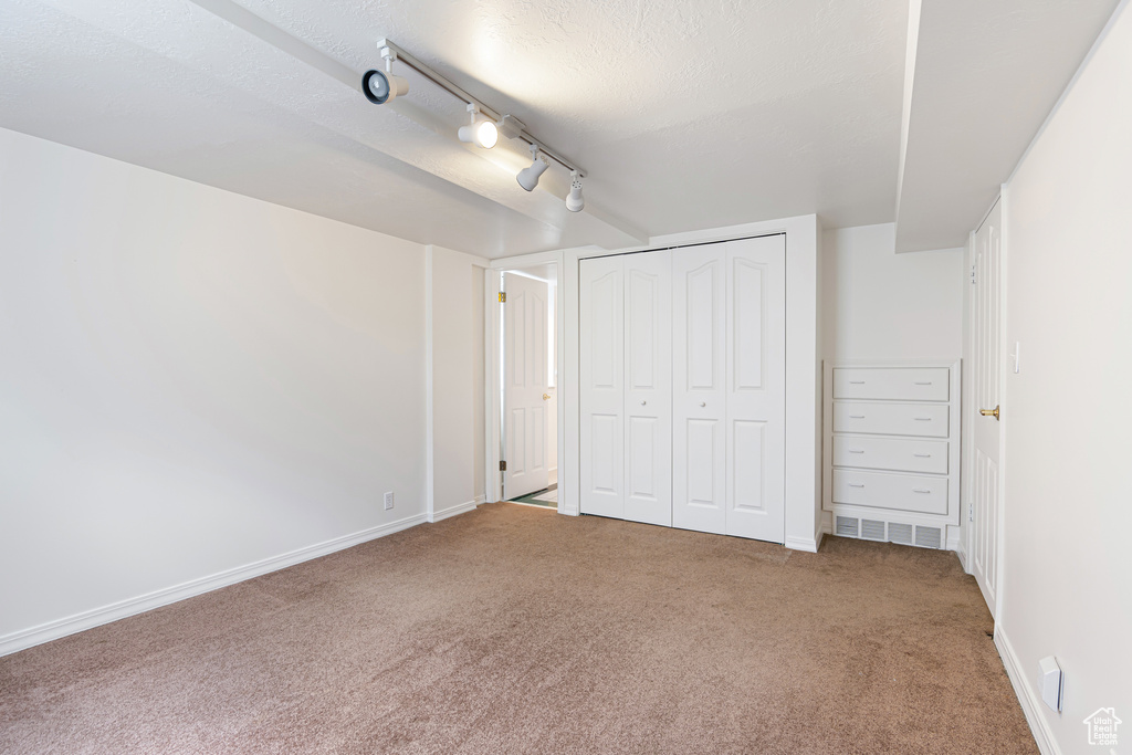 Unfurnished bedroom featuring carpet, rail lighting, baseboards, a closet, and a textured ceiling