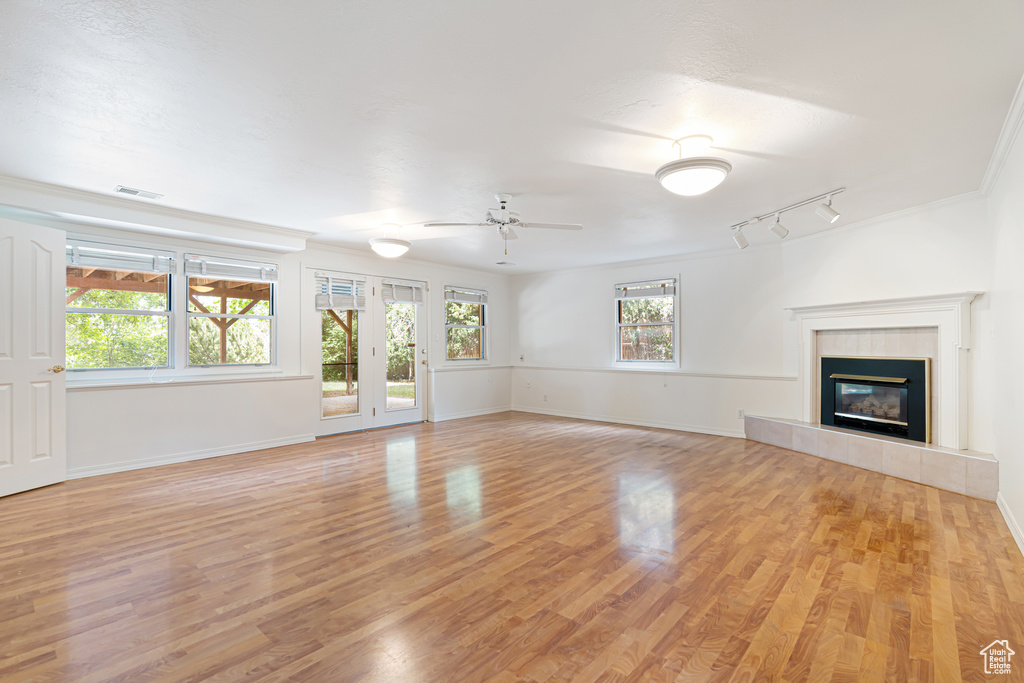 Unfurnished living room featuring ceiling fan, light wood-style flooring, a tiled fireplace, and baseboards