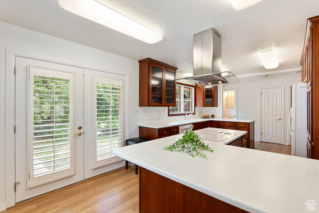 Kitchen featuring island exhaust hood, light wood-style floors, light countertops, french doors, and a textured ceiling