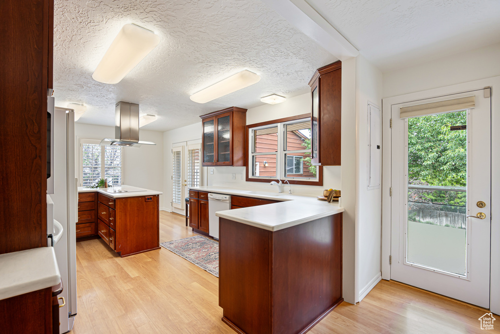 Kitchen featuring white appliances, a peninsula, island range hood, a sink, and light wood-style flooring