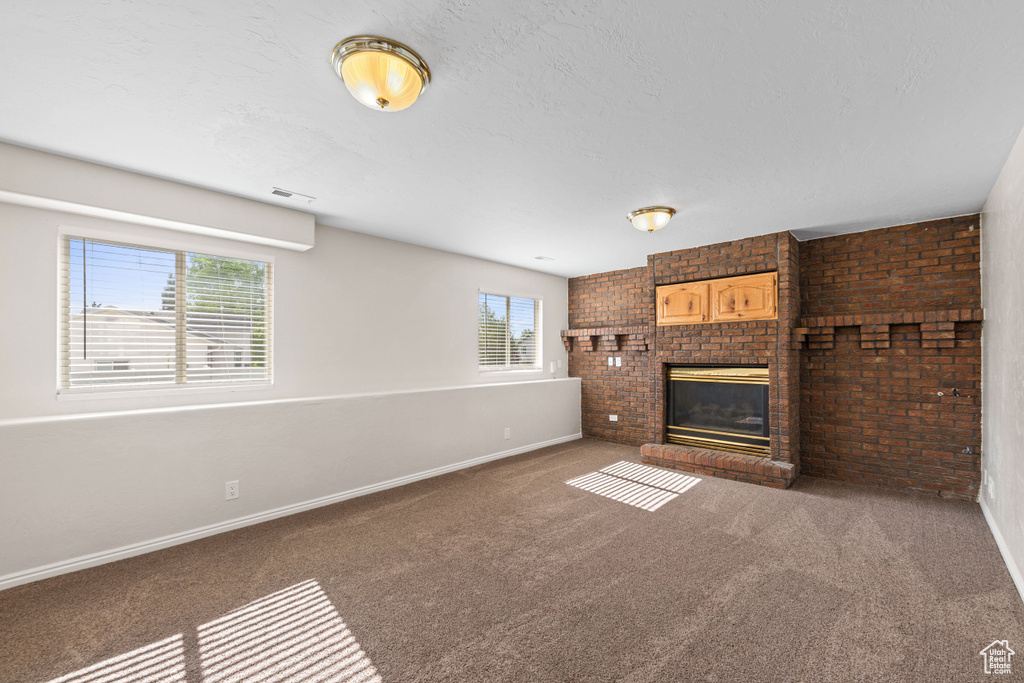 Unfurnished living room with baseboards, a brick fireplace, carpet flooring, and brick wall