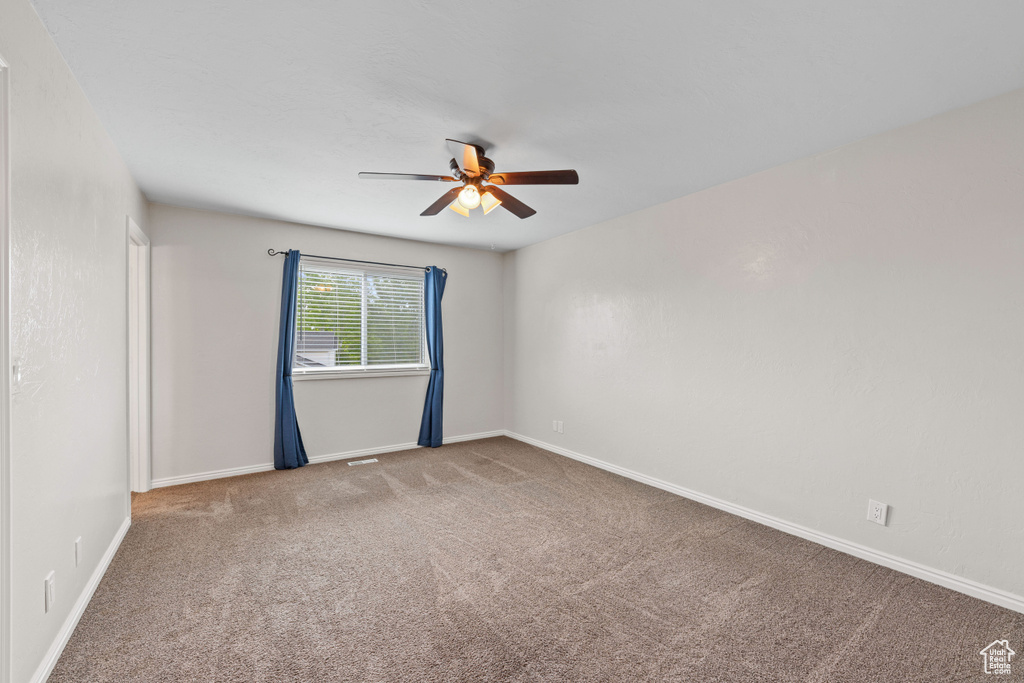 Carpeted empty room with a ceiling fan and baseboards