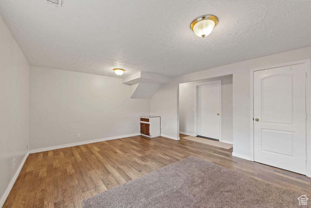 Additional living space with wood finished floors, baseboards, and a textured ceiling