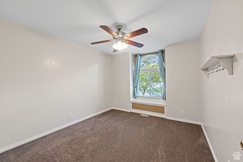 Unfurnished room featuring dark carpet, a ceiling fan, and baseboards