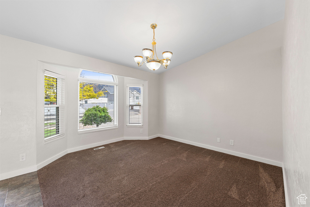 Unfurnished room with a chandelier, baseboards, and dark colored carpet