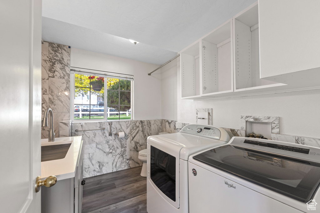 Clothes washing area with washing machine and clothes dryer, tile walls, dark wood-type flooring, and a wainscoted wall