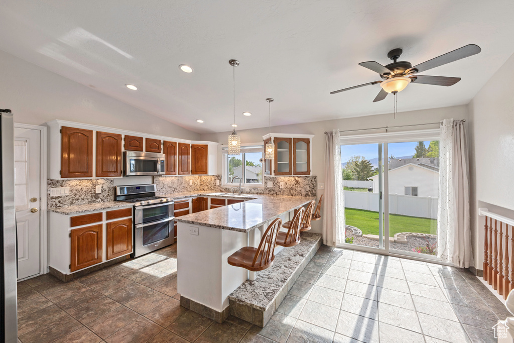 Kitchen featuring stainless steel appliances, a peninsula, decorative backsplash, a sink, and light stone countertops