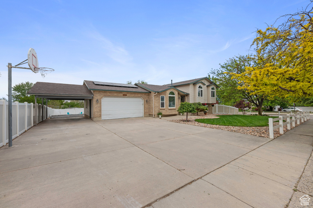 Split level home with brick siding, an attached garage, roof mounted solar panels, driveway, and a shingled roof
