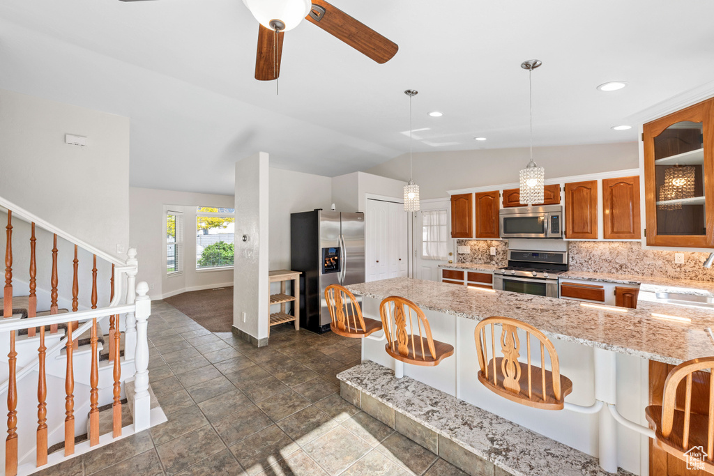 Kitchen featuring appliances with stainless steel finishes, baseboards, vaulted ceiling, brown cabinetry, and tasteful backsplash