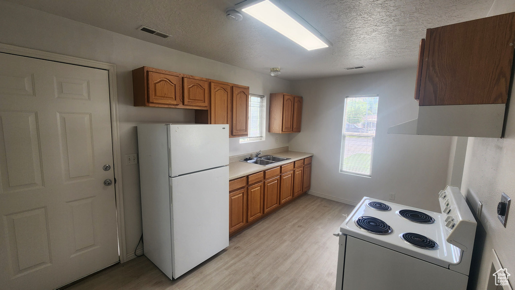 Kitchen with white appliances, a sink, a textured ceiling, light countertops, and light wood-style flooring