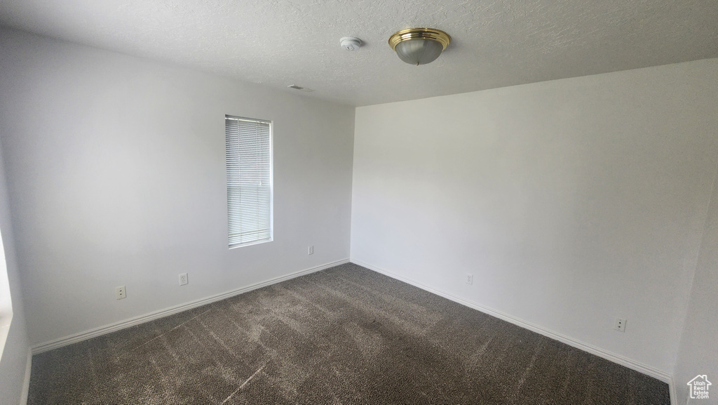 Unfurnished room with dark carpet, a textured ceiling, and baseboards