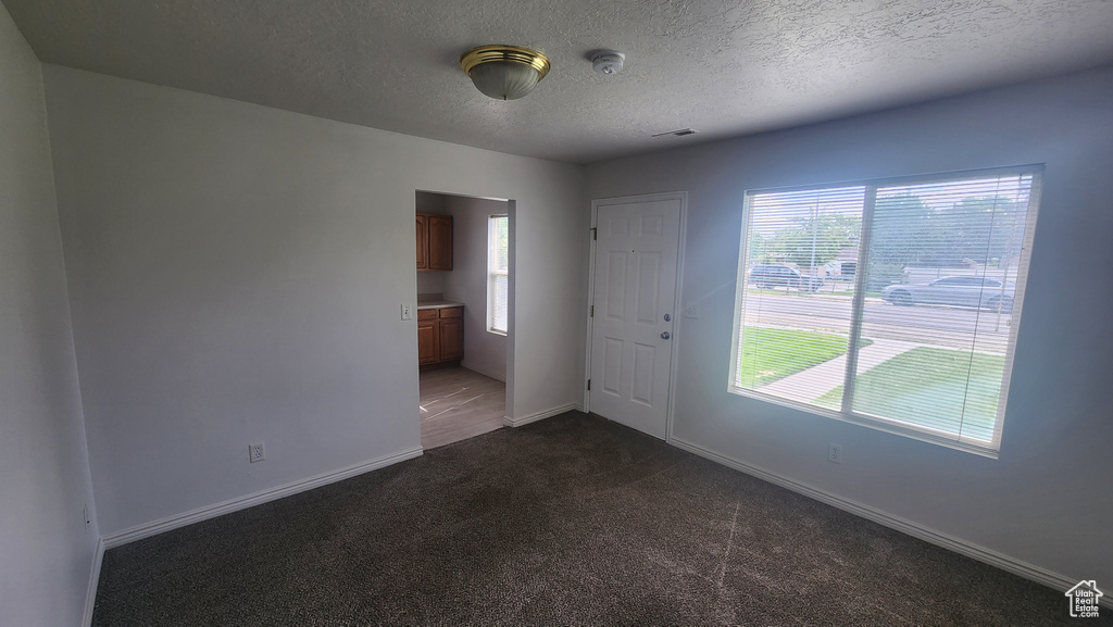 Unfurnished room with dark colored carpet, a textured ceiling, baseboards, and a smoke detector