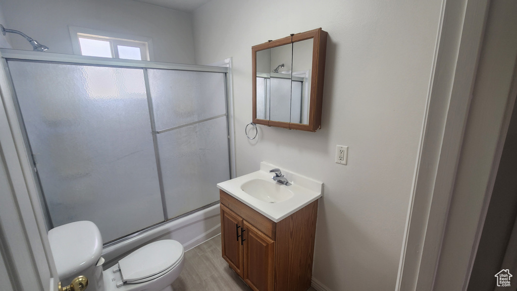 Bathroom featuring vanity, toilet, bath / shower combo with glass door, and wood finished floors